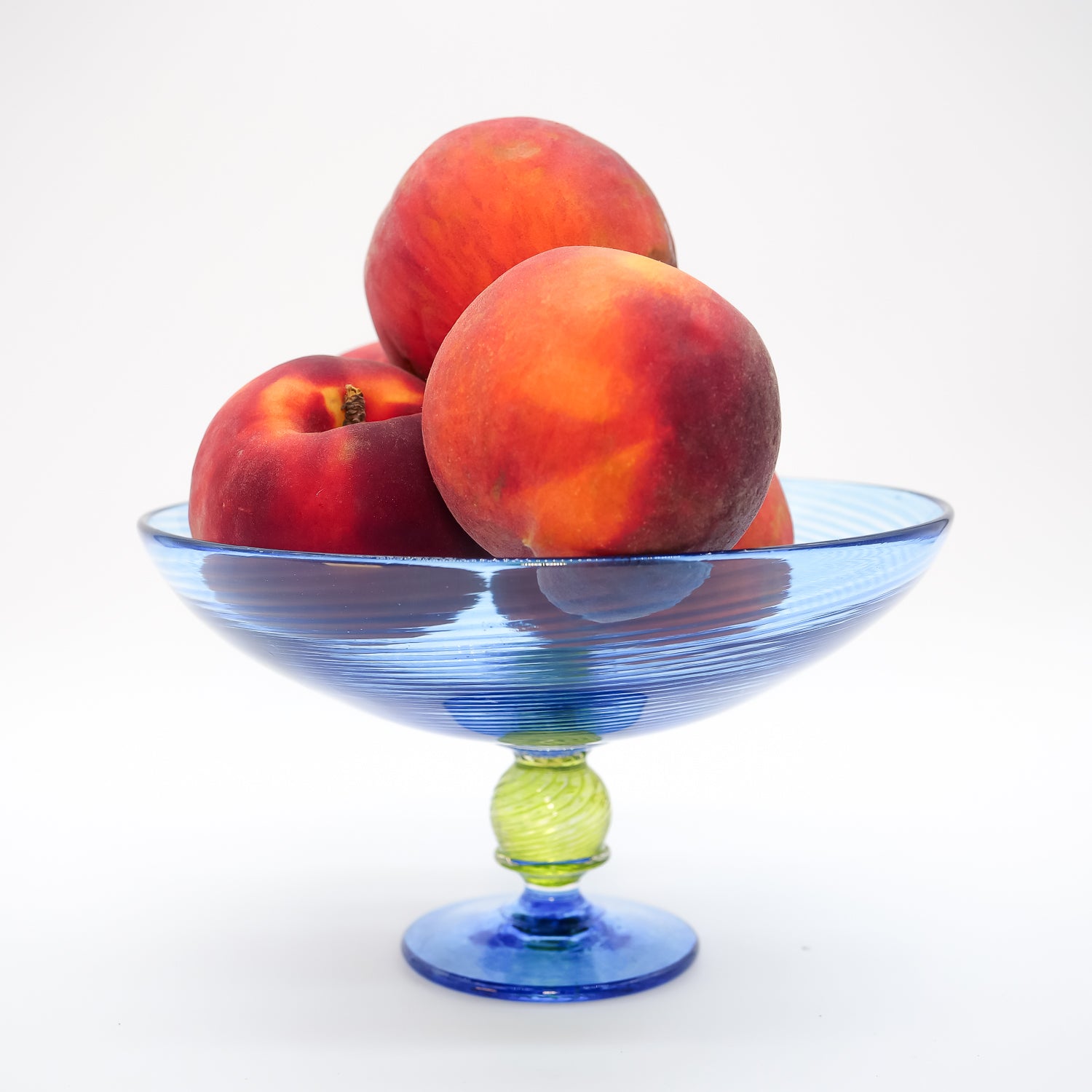 Colorful blue handblown glass trifle bowl with peaches on a white background