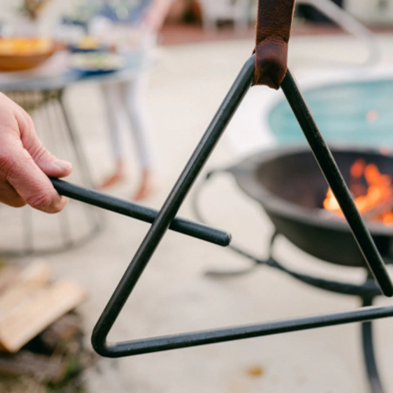 Person holding a black metal trianglular dinner bell over a fire pit.