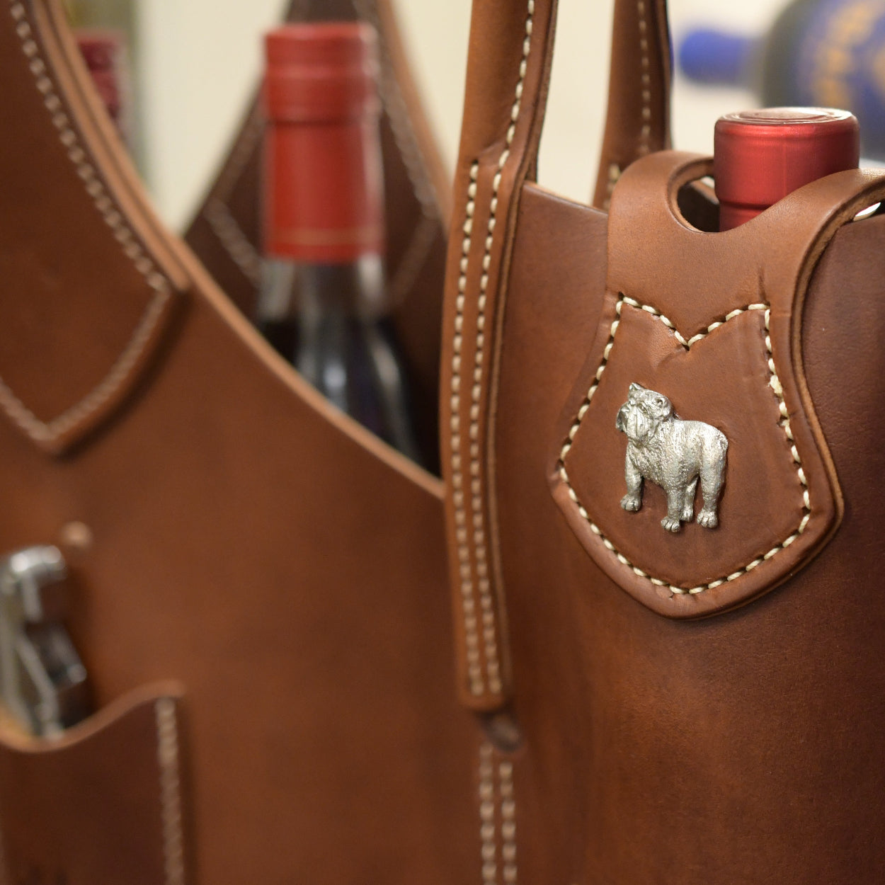 Brown leather wine carrier with a bulldog emblem and two bottles inside.