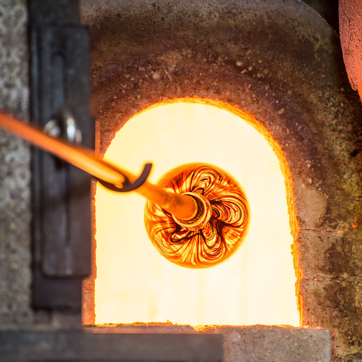 Glassblowing process with a hot glass orb and tool inside a furnace.