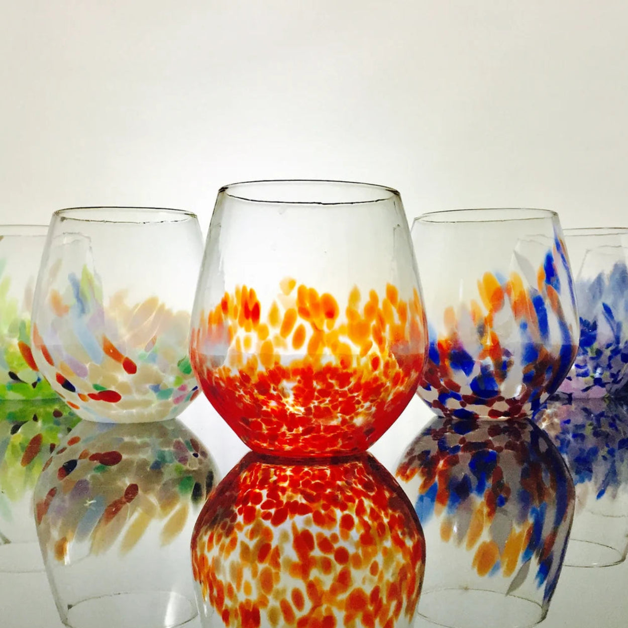 Set of colorful glass tumblers on a reflective surface with a white background
