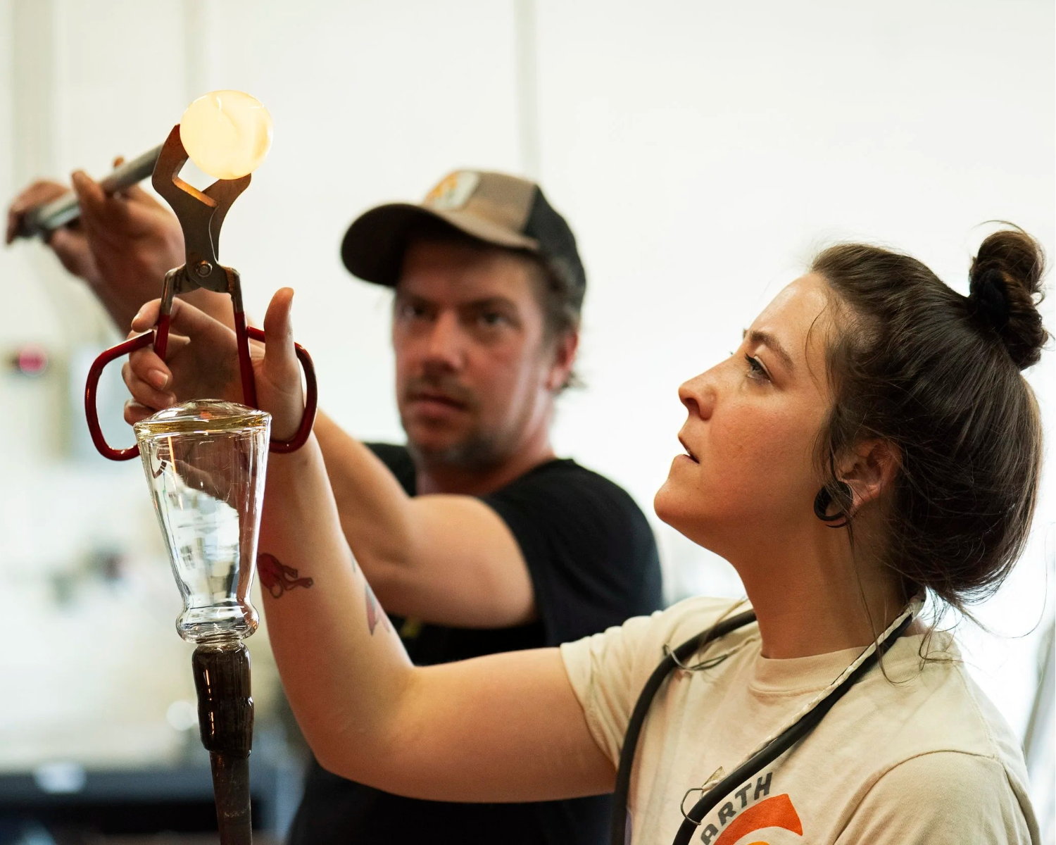 Two people working with glassblowing tools in a workshop setting.