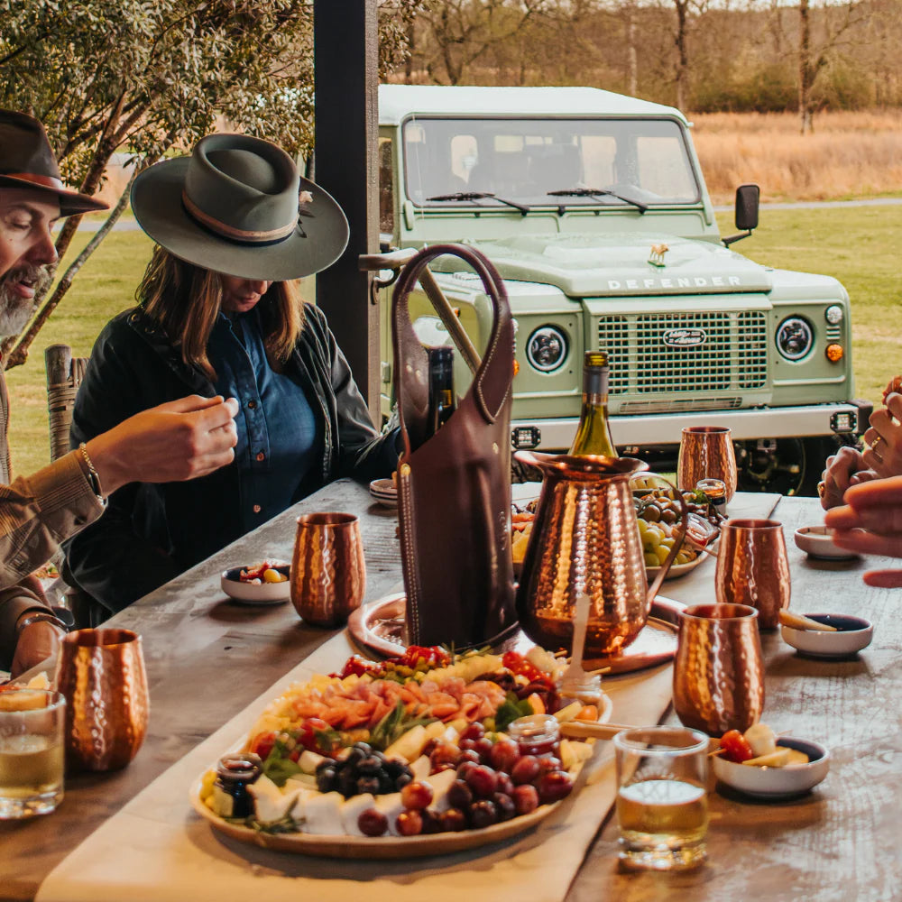 Two people enjoying a meal outdoors with a Land Rover vehicle in the background and a meal with a wine tote on the table