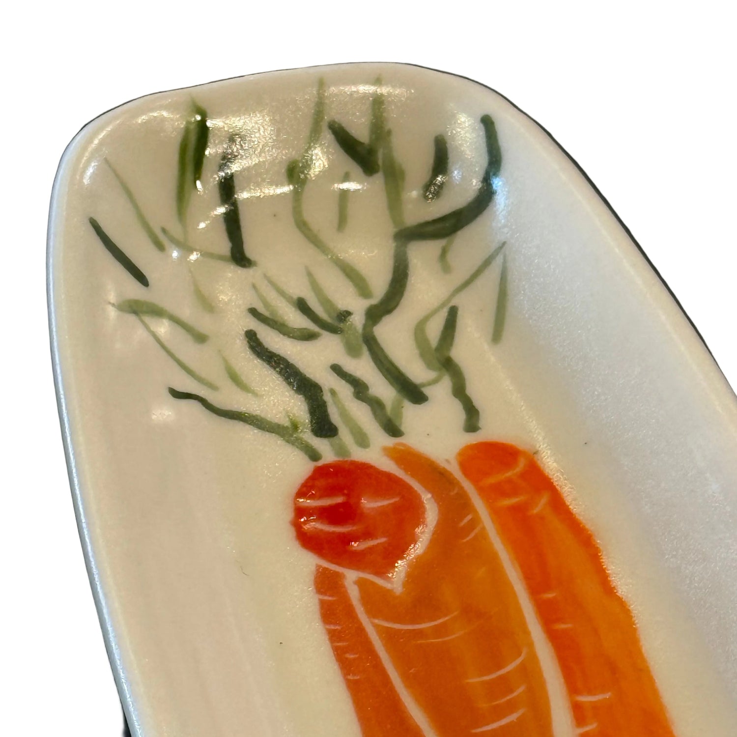 A close-up of a white ceramic plate featuring a painted design of orange carrots with green leafy tops