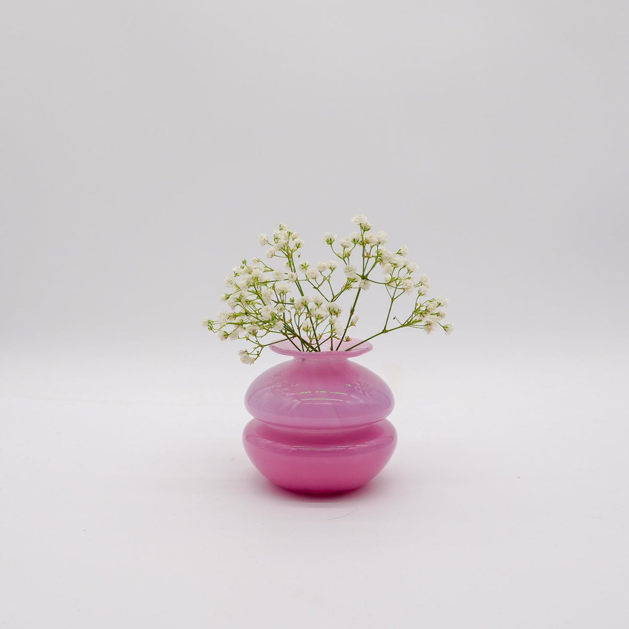 Pink vase with small green flowers on a light gray background