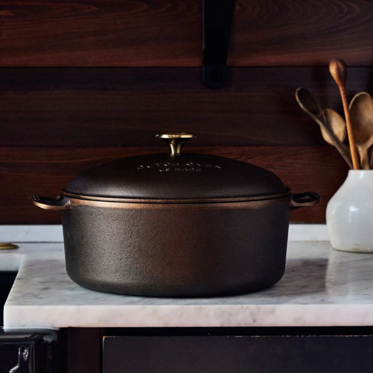 Cast iron Smithey Dutch Ovent on a marble countertop with wooden utensils in the background.