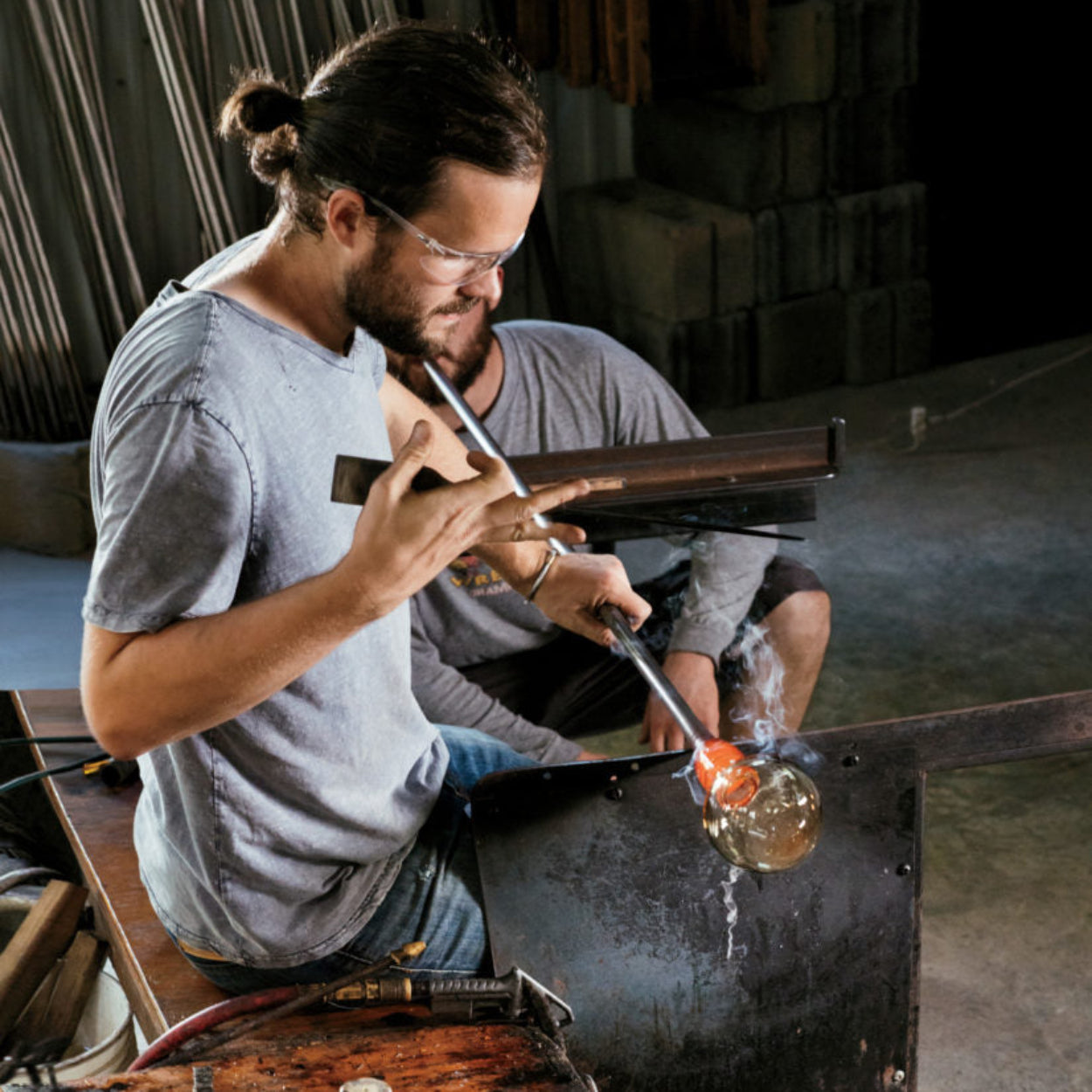 Glassblower shaping molten glass in a workshop setting