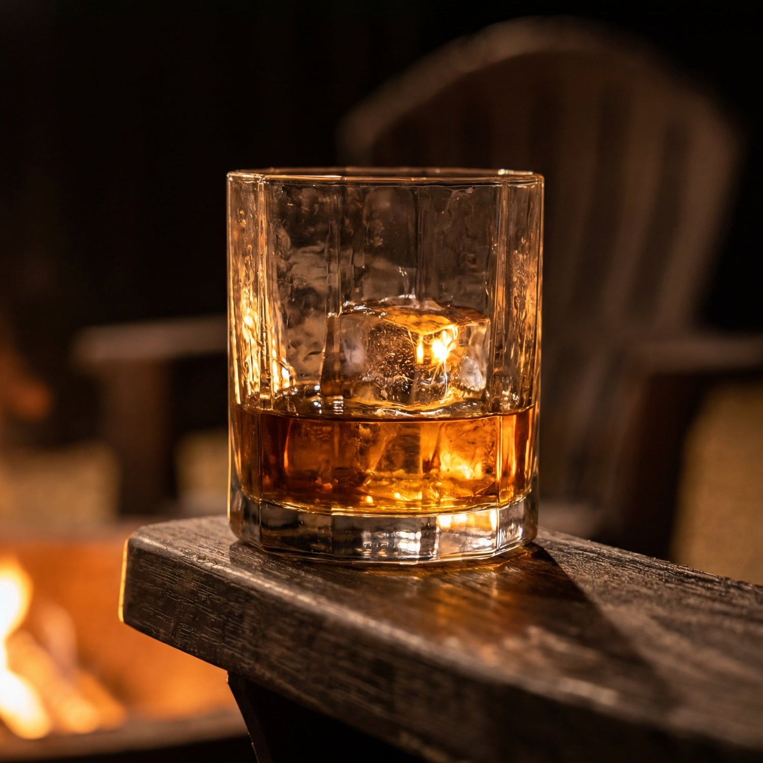 Terrane Glass No 12 Rocks Glass with bourbon and ice on a wooden chair arm in front of an outdoor fire pit.