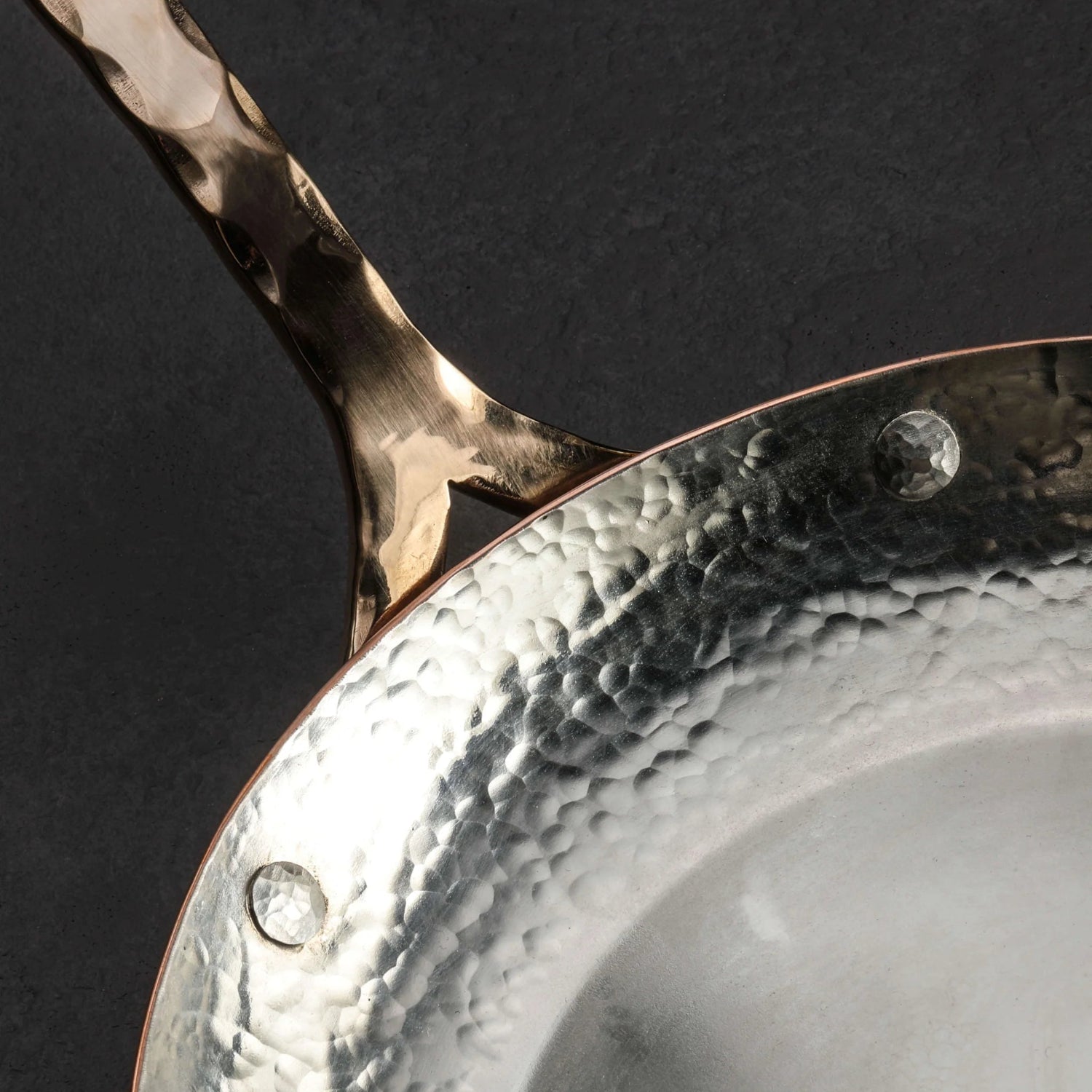 Close-up of a copper frying pan with a textured handle on a dark background