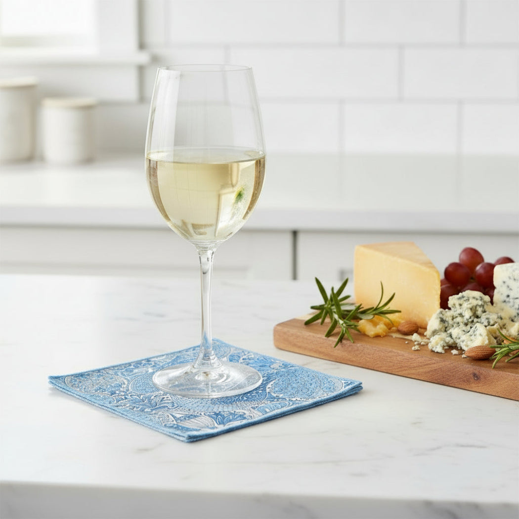 Glass of white wine on a blue napkin with a cheeseboard in the background