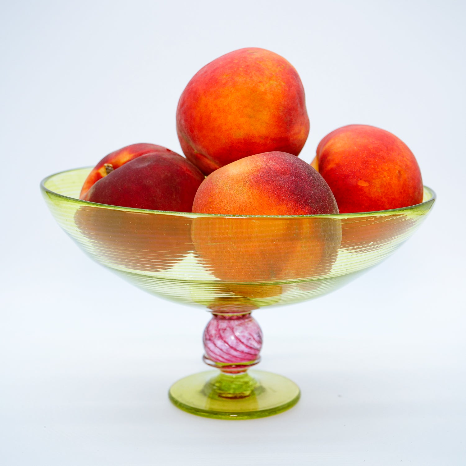 Colorful handblown chartruese glass trifle bowl with peaches on a white background