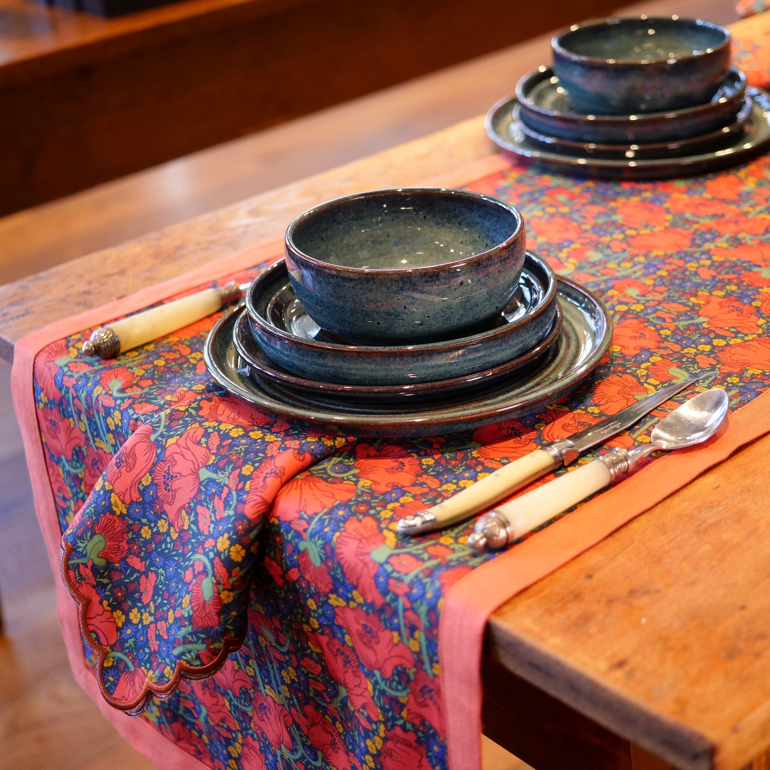 Dinnerware set on a wooden table with a colorful floral Liberty Clementina Poppy tablecloth