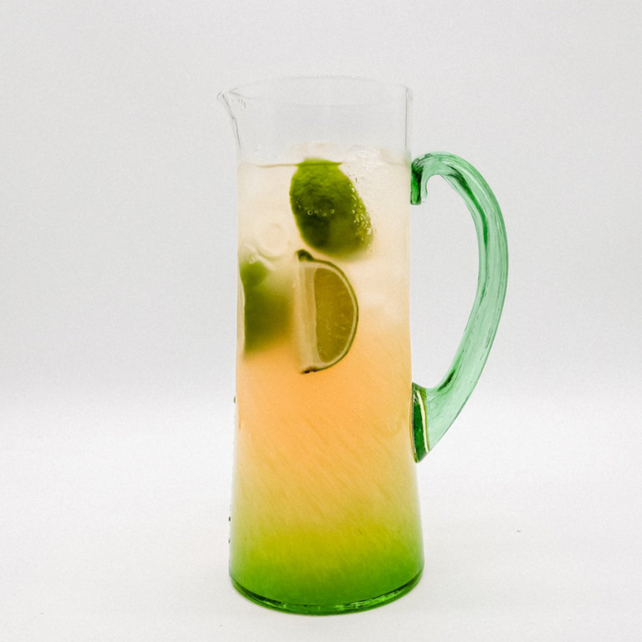 Glass pitcher with green handle filled with a margarita on a white background