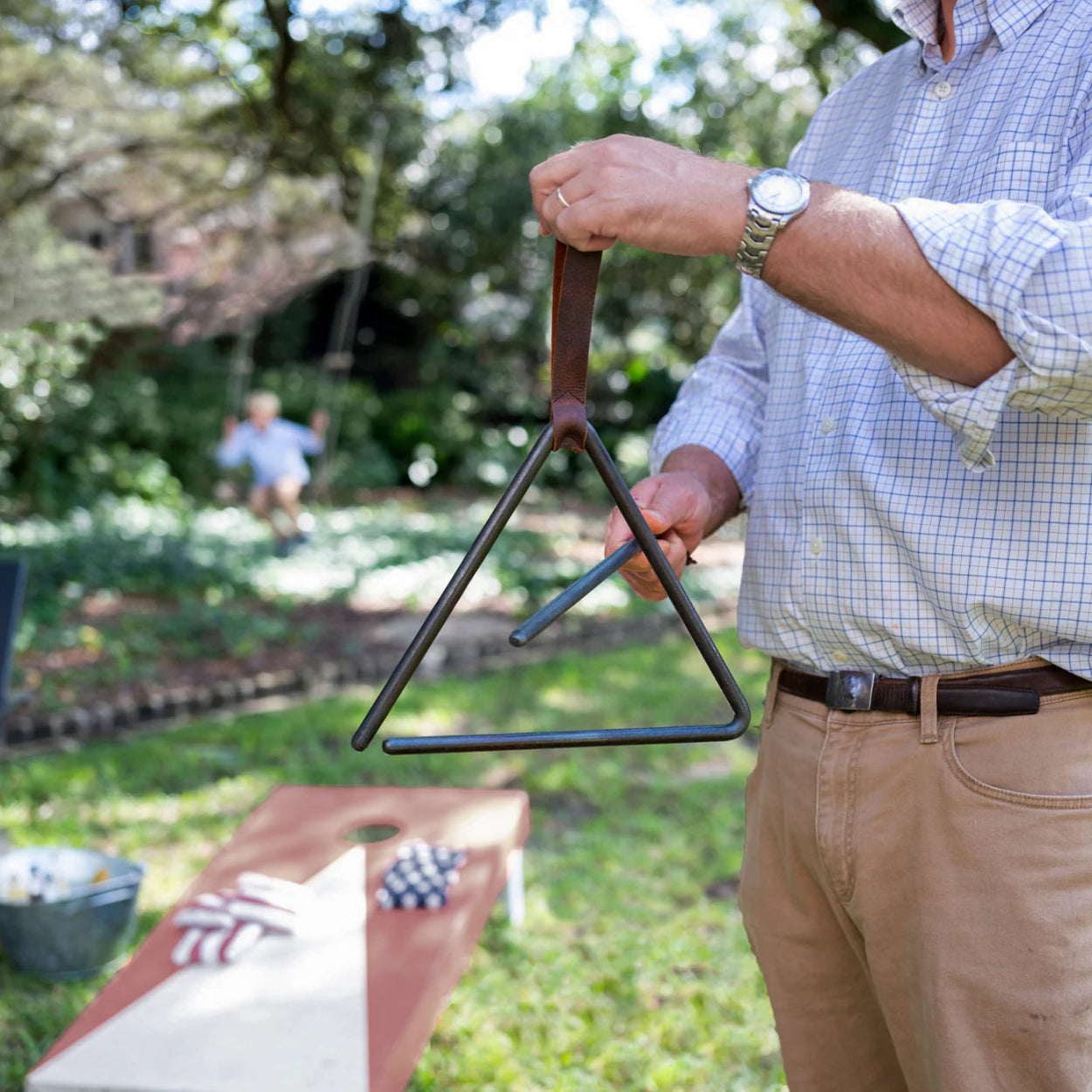 Man holding a trinagular dinner bell summoning his family to a meal.