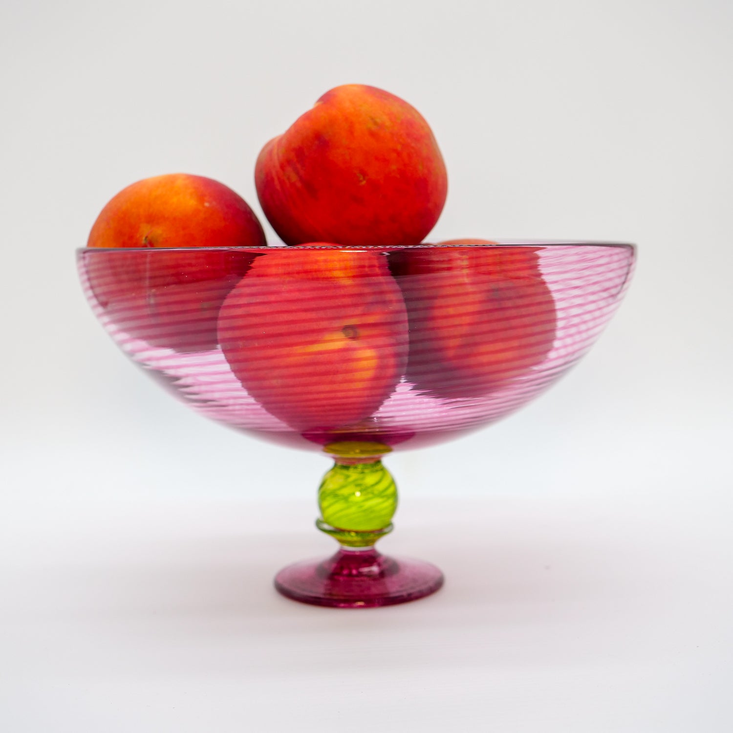 Colorful handblown glass trifle bowl with peaches on a white background
