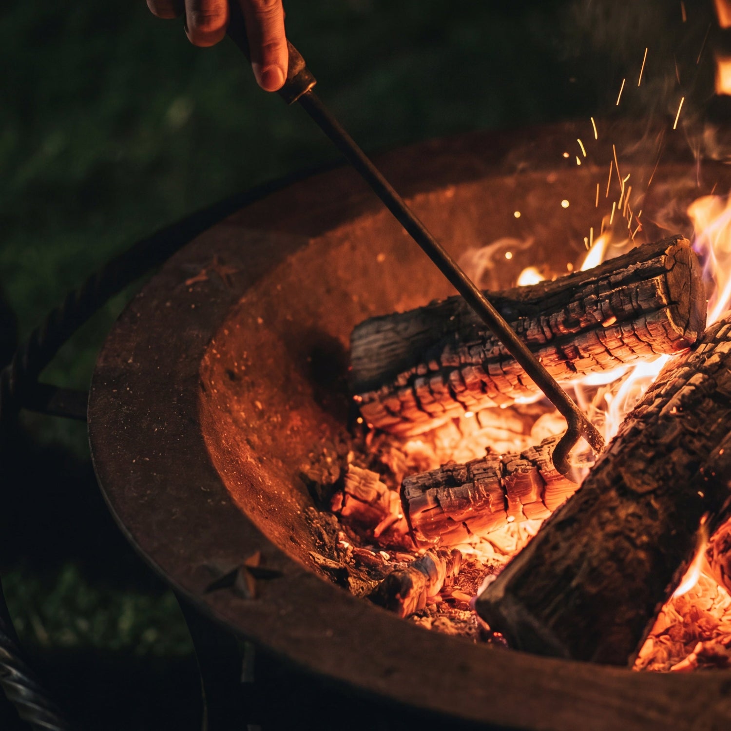 Person adjusting a fire in a Sea Island Forge fire pit with a poker.