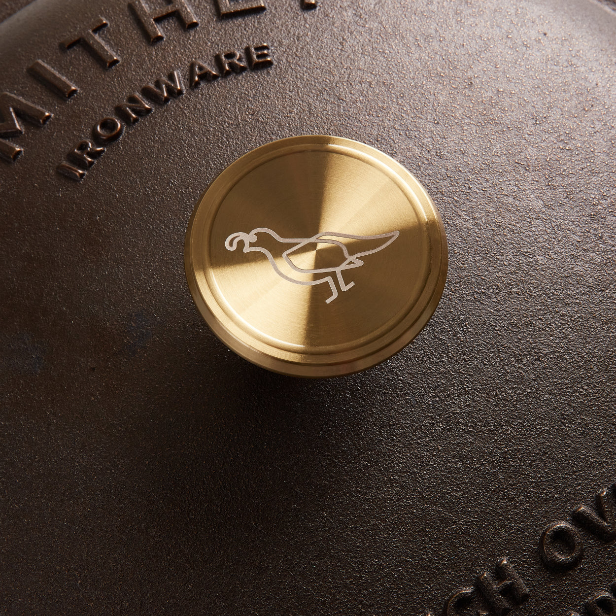 Close-up of a gold handle with a logo on a cast iron dutch oven, featuring the brand name 'Smithey Ironware'.