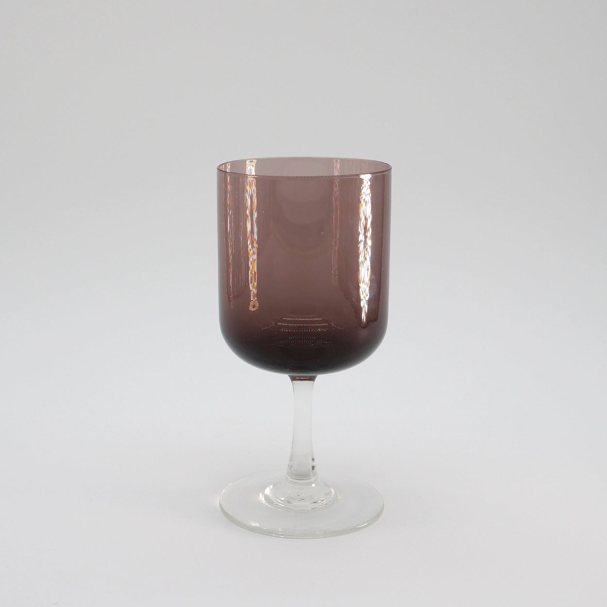 A hand-blown aubergine-colored stemware glass with a clear stem and base, displayed against a white background.