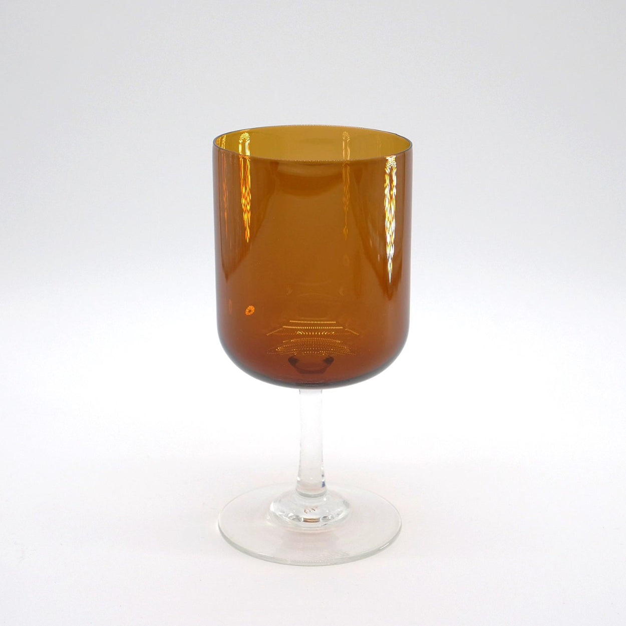 A hand-blown amber-colored stemware glass with a clear stem and base, displayed against a white background.