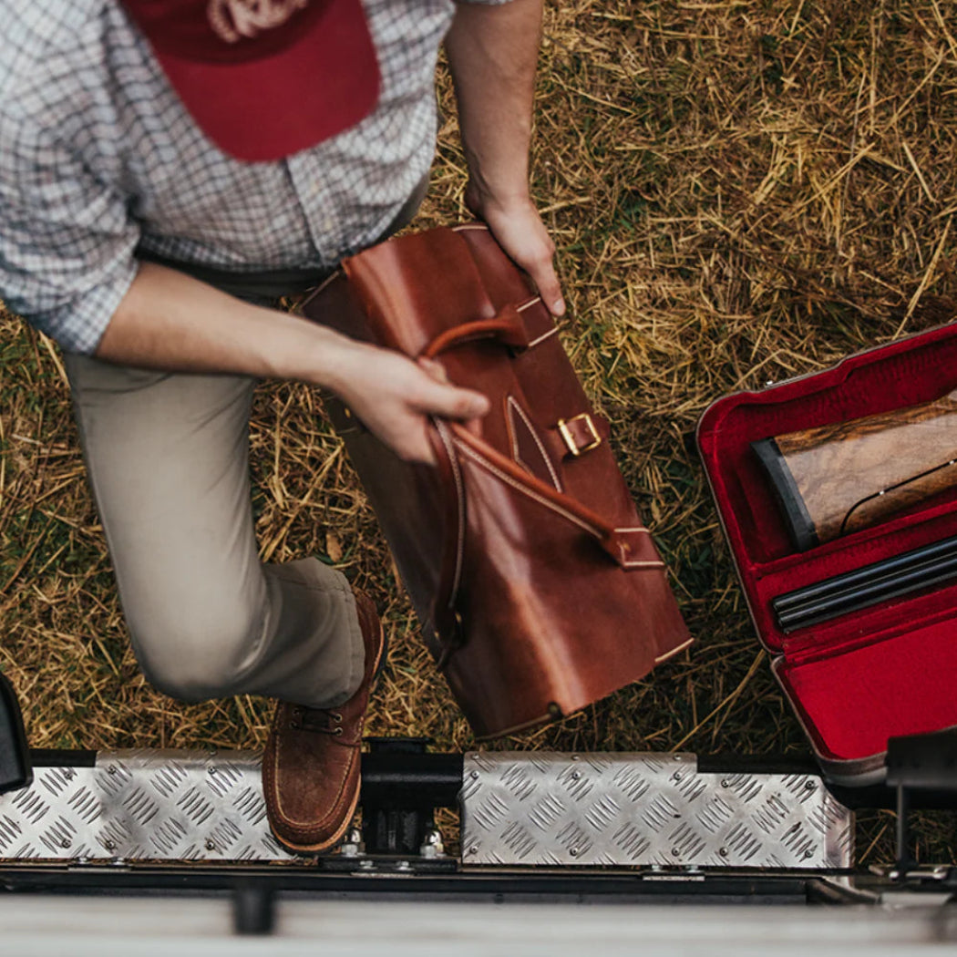 Person placing a  leather weekender bag into a truck.