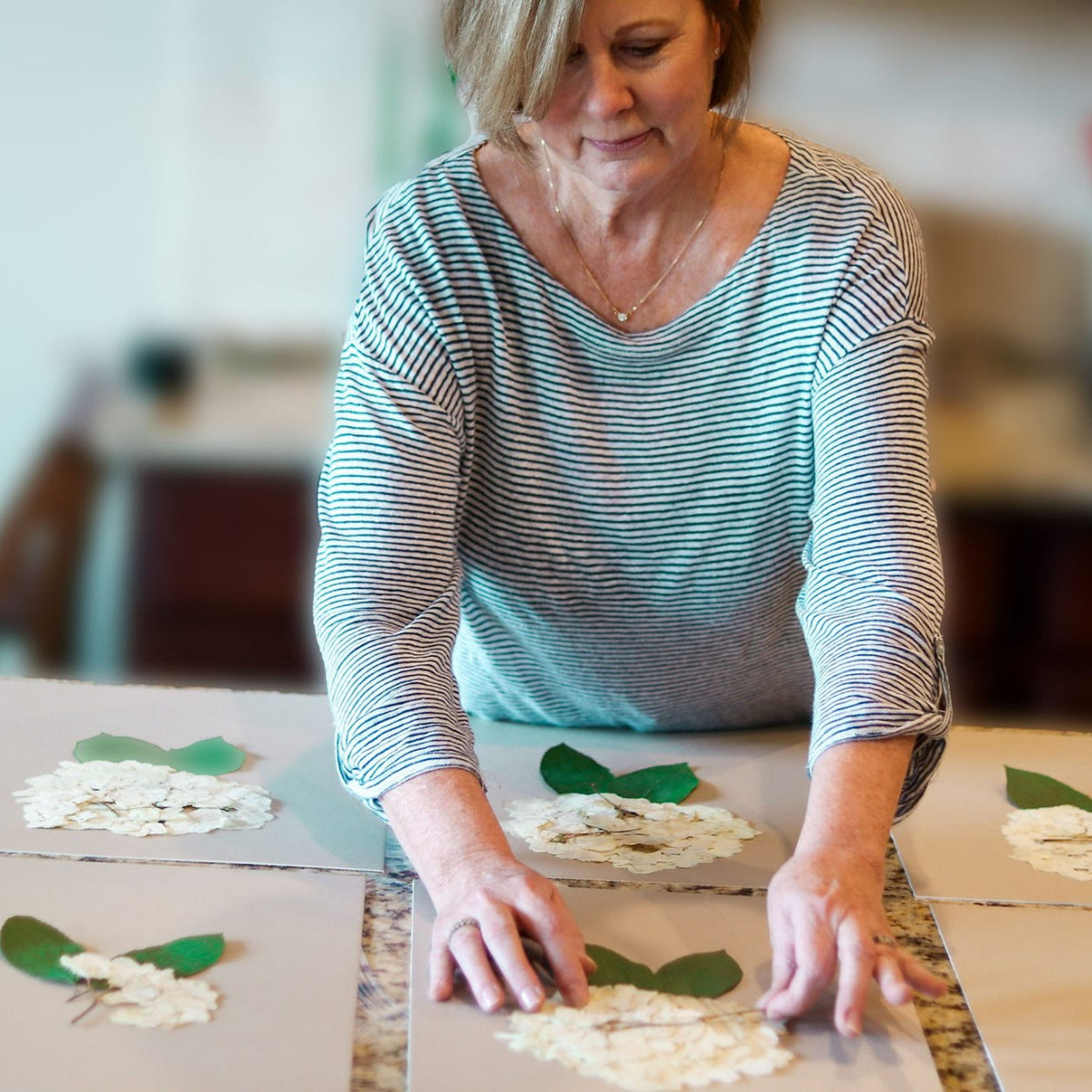 Sandy Whitaker arranging pressed hydrangea blossoms and leaves by hand on backing boards in her Cartersville, Georgia studio